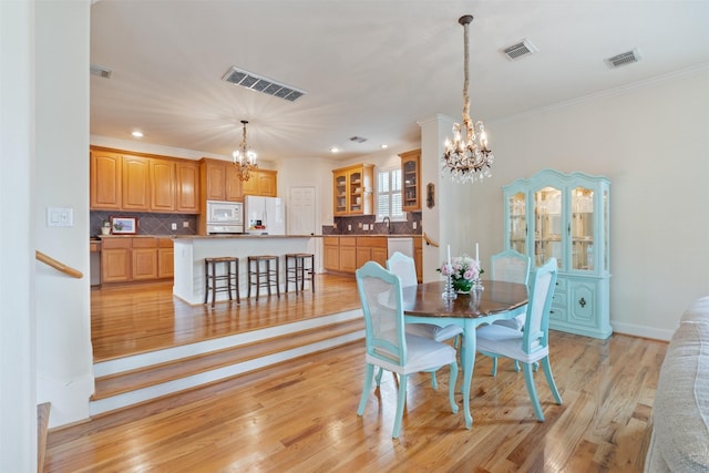 dining room with a notable chandelier, ornamental molding, sink, and light wood-type flooring