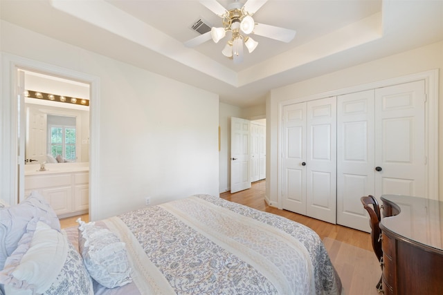 bedroom with light hardwood / wood-style flooring, ceiling fan, ensuite bathroom, a raised ceiling, and a closet