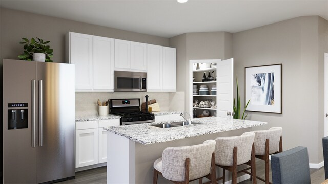 kitchen with sink, light stone counters, appliances with stainless steel finishes, an island with sink, and white cabinets