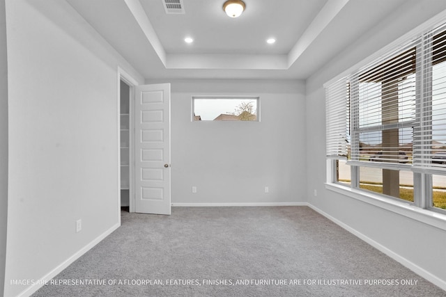 empty room with carpet, a raised ceiling, baseboards, and visible vents