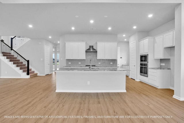 kitchen featuring white cabinetry, light wood-style flooring, an island with sink, and appliances with stainless steel finishes