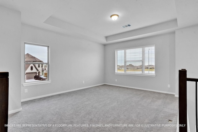 unfurnished room with a tray ceiling, visible vents, baseboards, and carpet