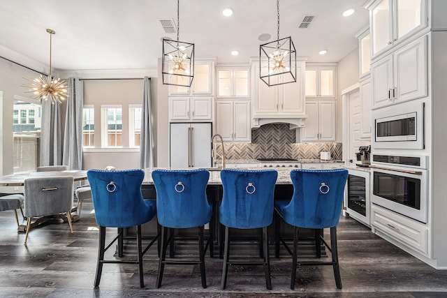 kitchen with stainless steel microwave, an island with sink, hanging light fixtures, light stone counters, and white oven