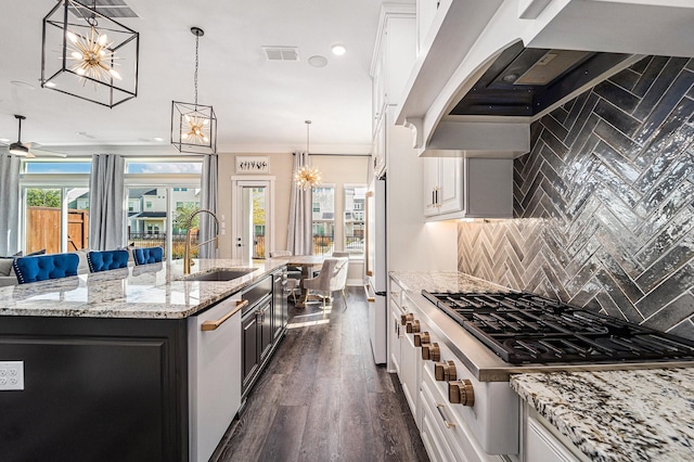 kitchen featuring stainless steel gas cooktop, custom exhaust hood, a center island with sink, white refrigerator, and white cabinets