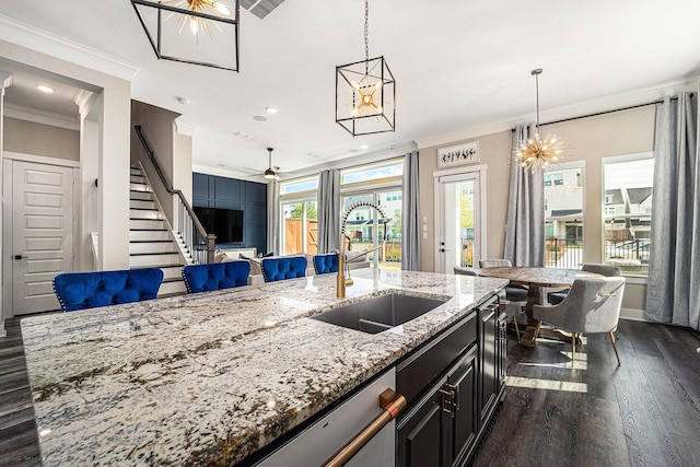 kitchen featuring sink, crown molding, hanging light fixtures, light stone countertops, and an island with sink