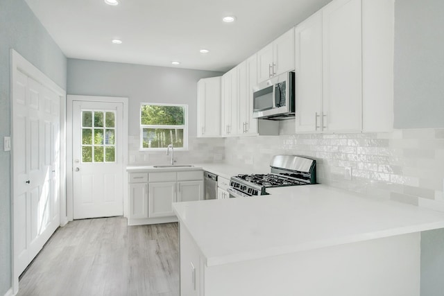 kitchen with appliances with stainless steel finishes, kitchen peninsula, sink, and white cabinets