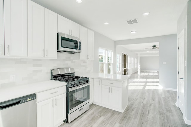 kitchen with tasteful backsplash, stainless steel appliances, kitchen peninsula, and white cabinets