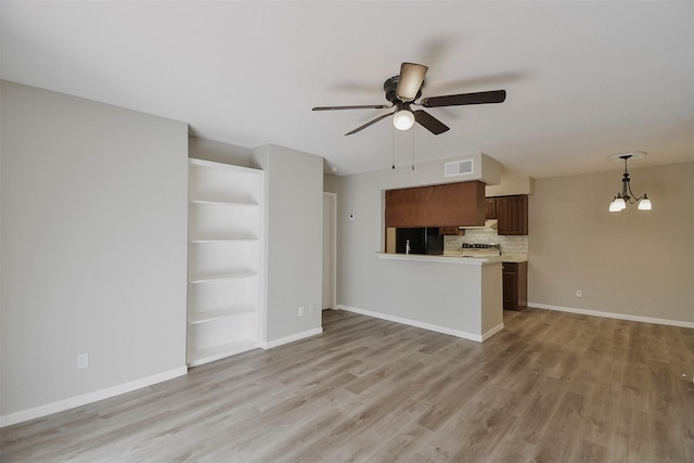 unfurnished living room with ceiling fan with notable chandelier and light wood-type flooring