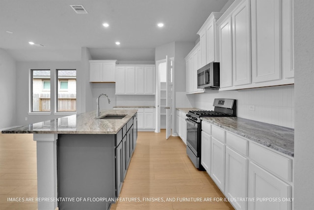 kitchen featuring visible vents, light wood-type flooring, stainless steel appliances, white cabinetry, and a sink