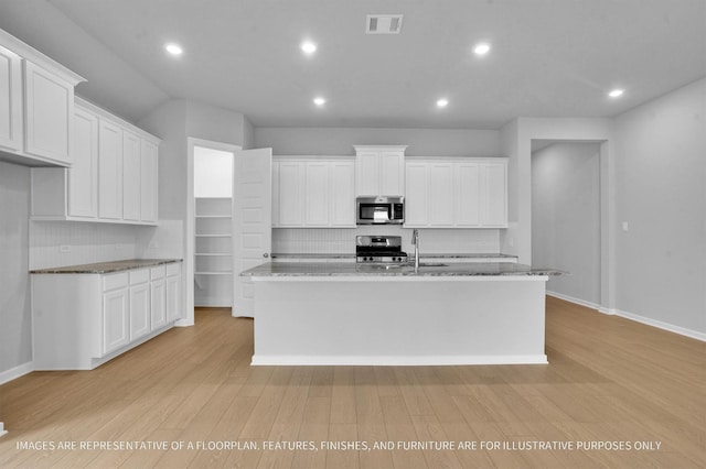 kitchen featuring visible vents, a kitchen island with sink, a sink, stainless steel appliances, and light wood-style floors