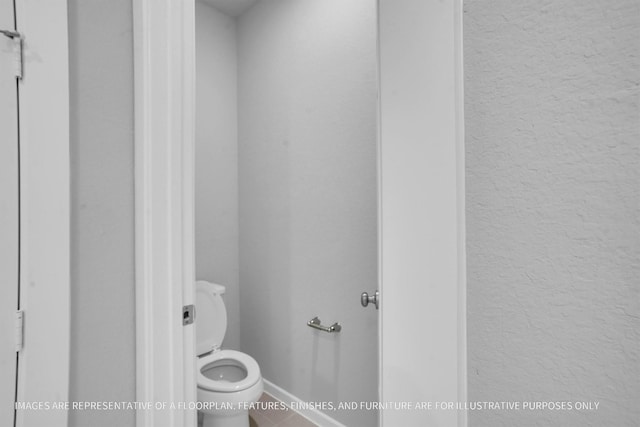 bathroom featuring toilet, a textured wall, and baseboards