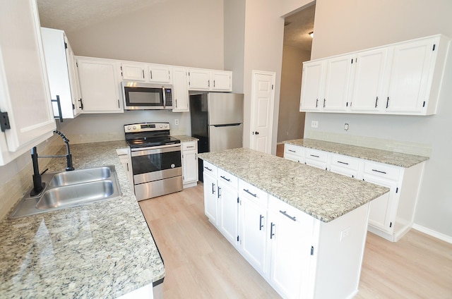 kitchen with sink, appliances with stainless steel finishes, white cabinetry, a center island, and light hardwood / wood-style floors