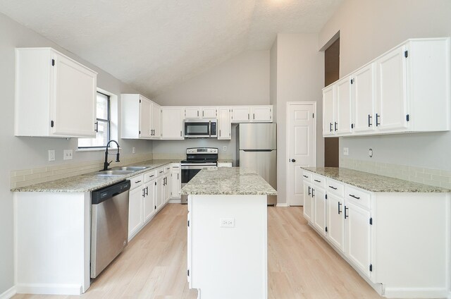 kitchen with white cabinetry, light stone counters, stainless steel appliances, and a center island