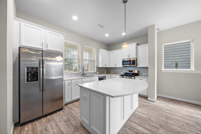 kitchen with stainless steel appliances, white cabinetry, a center island, and decorative light fixtures