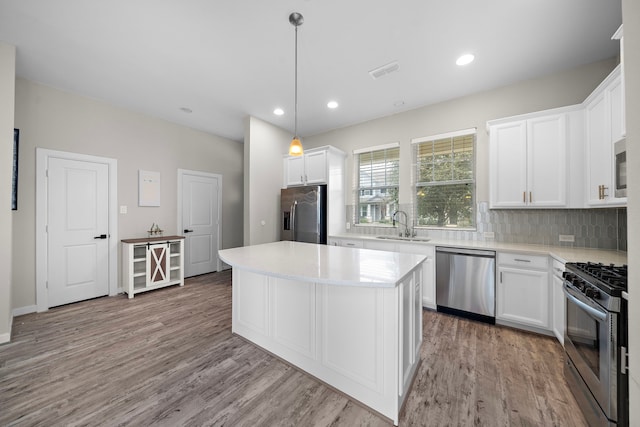 kitchen featuring appliances with stainless steel finishes, pendant lighting, white cabinetry, sink, and a center island