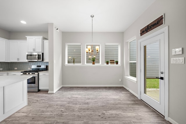 kitchen with white cabinetry, an inviting chandelier, decorative light fixtures, light wood-type flooring, and stainless steel appliances