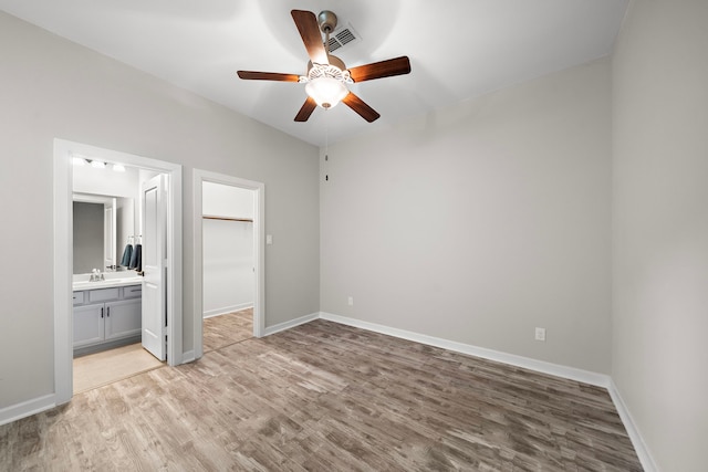 unfurnished bedroom with sink, a walk in closet, ensuite bath, light wood-type flooring, and ceiling fan