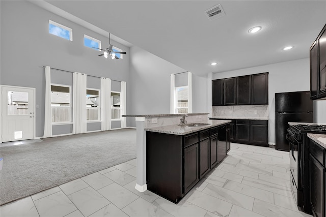 kitchen with sink, dark brown cabinetry, black appliances, light carpet, and a center island with sink