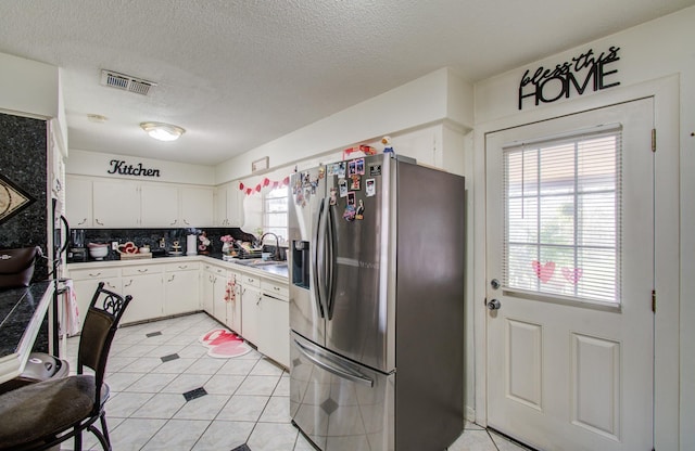 kitchen featuring tasteful backsplash, white cabinetry, sink, stainless steel fridge, and a textured ceiling