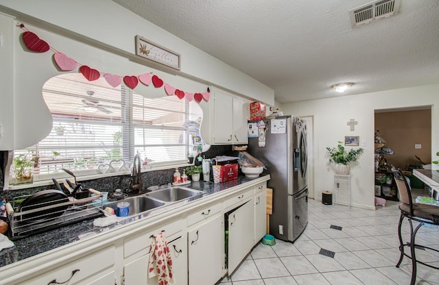 kitchen featuring sink, light tile patterned floors, white cabinetry, stainless steel refrigerator with ice dispenser, and a textured ceiling