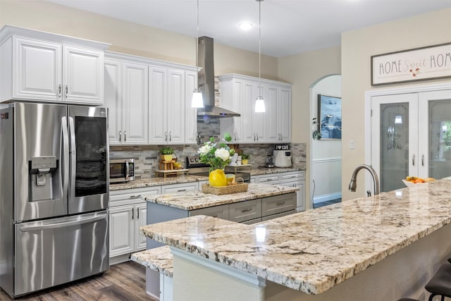 kitchen with wall chimney exhaust hood, appliances with stainless steel finishes, decorative light fixtures, and white cabinets