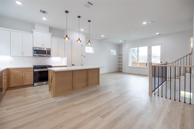 kitchen featuring appliances with stainless steel finishes, white cabinetry, a center island, decorative light fixtures, and light wood-type flooring