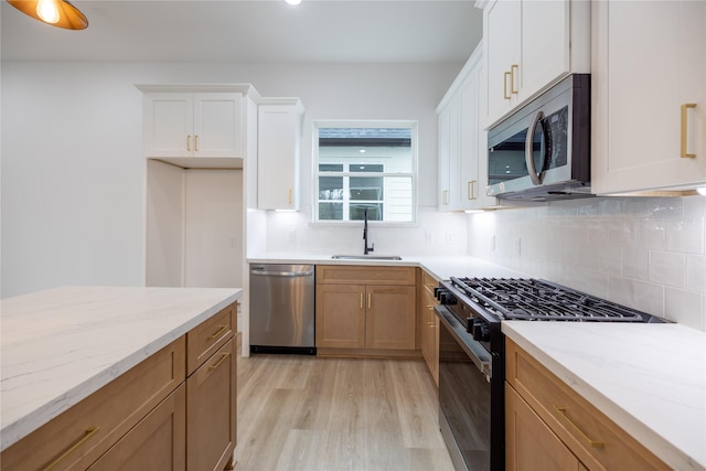 kitchen featuring sink, light hardwood / wood-style flooring, appliances with stainless steel finishes, white cabinetry, and light stone countertops