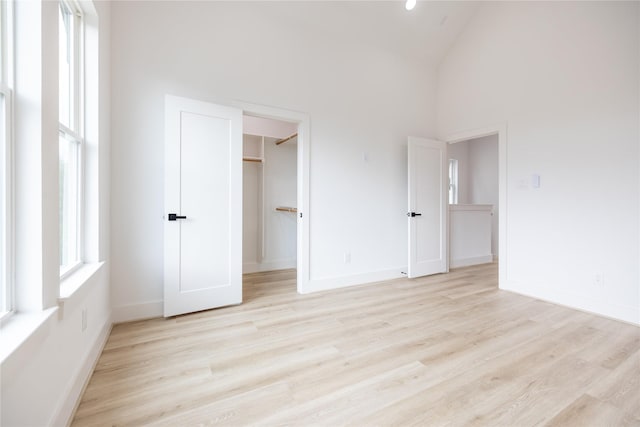 unfurnished bedroom featuring a closet, a spacious closet, high vaulted ceiling, and light hardwood / wood-style floors