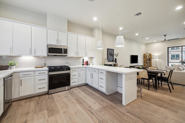 kitchen with appliances with stainless steel finishes, white cabinetry, hanging light fixtures, kitchen peninsula, and light wood-type flooring