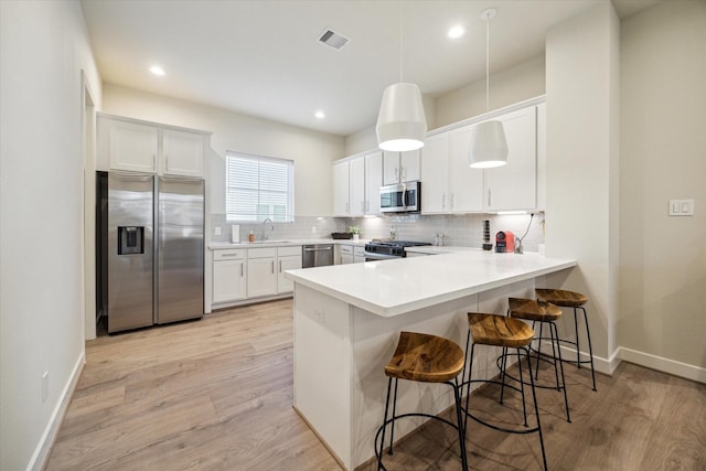 kitchen with sink, appliances with stainless steel finishes, white cabinetry, decorative light fixtures, and kitchen peninsula