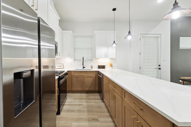 kitchen with sink, light stone counters, pendant lighting, stainless steel appliances, and white cabinets