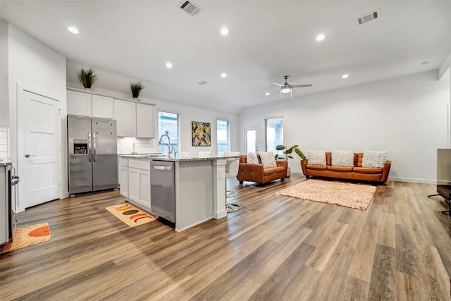 kitchen with sink, white cabinetry, appliances with stainless steel finishes, an island with sink, and light stone countertops