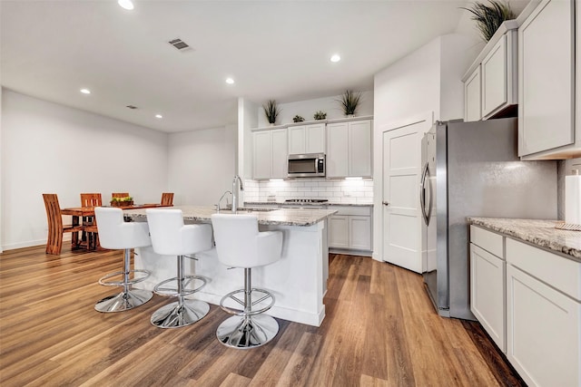 kitchen featuring appliances with stainless steel finishes, white cabinetry, light stone counters, a center island with sink, and light hardwood / wood-style flooring