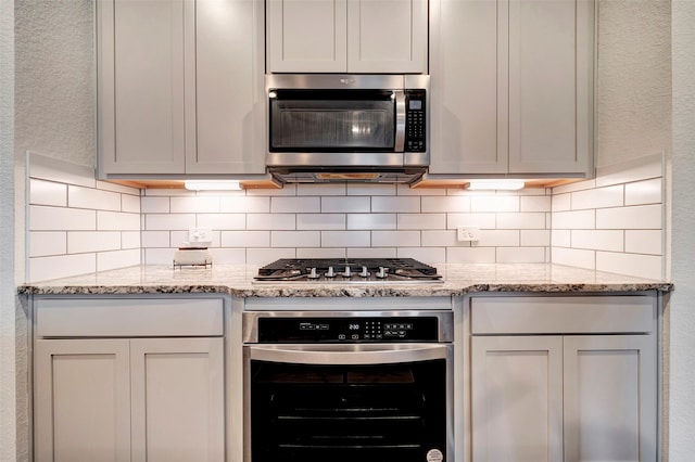 kitchen with light stone countertops, backsplash, and stainless steel appliances