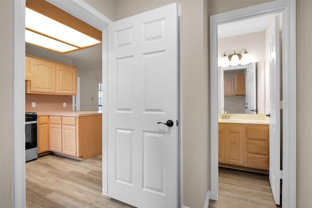 kitchen featuring light brown cabinetry, sink, stainless steel range oven, and light wood-type flooring