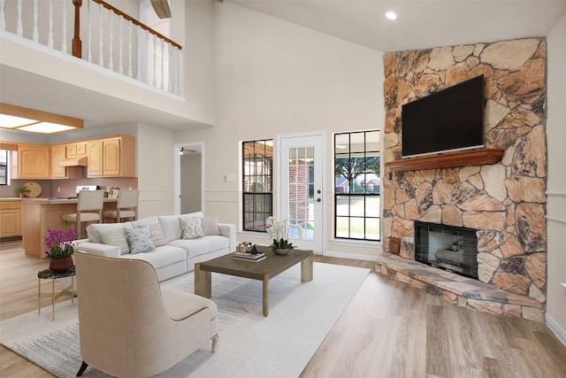 living room with a stone fireplace, light hardwood / wood-style flooring, and high vaulted ceiling