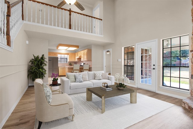 living room with ceiling fan, a towering ceiling, light hardwood / wood-style floors, and a healthy amount of sunlight