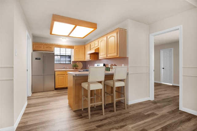 kitchen with hardwood / wood-style flooring, a breakfast bar area, high quality fridge, kitchen peninsula, and light brown cabinets