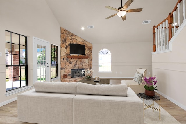 living room with ceiling fan, high vaulted ceiling, a stone fireplace, and light hardwood / wood-style floors