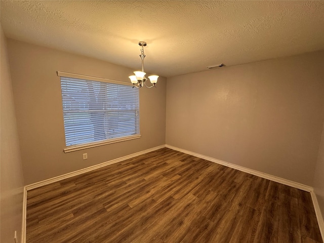 spare room featuring an inviting chandelier, dark hardwood / wood-style floors, and a textured ceiling