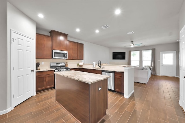 kitchen featuring sink, ceiling fan, appliances with stainless steel finishes, light stone counters, and kitchen peninsula