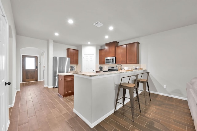 kitchen featuring light stone countertops, stainless steel appliances, a breakfast bar, and kitchen peninsula