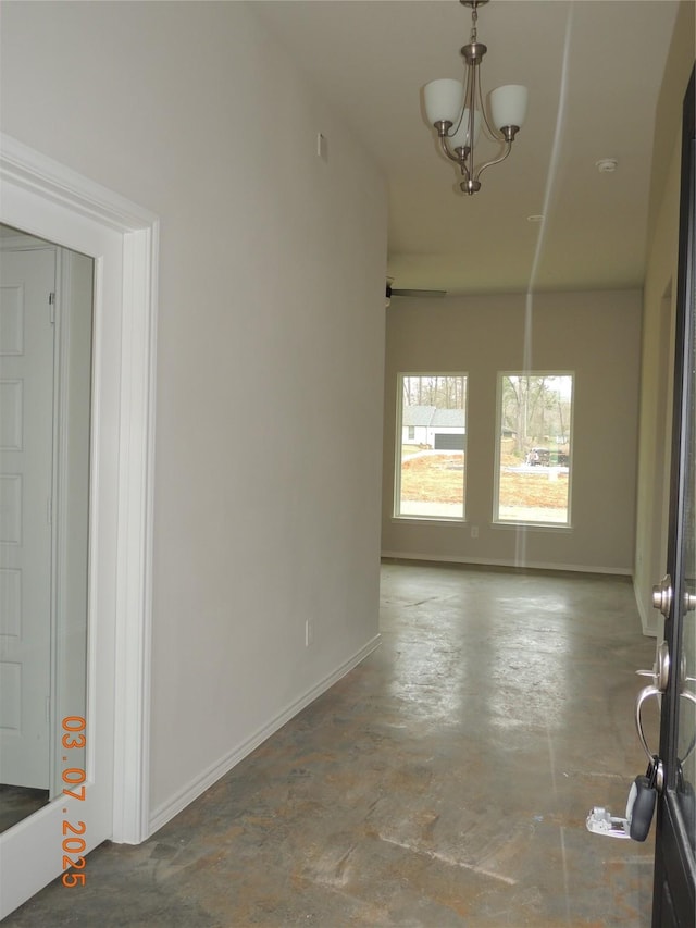 spare room with concrete floors, an inviting chandelier, and baseboards