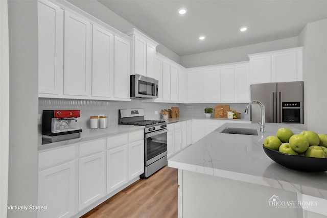 kitchen featuring white cabinets, stainless steel appliances, light wood-style floors, and a sink