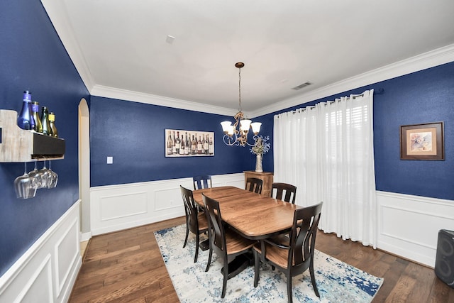 dining area featuring dark wood-type flooring, ornamental molding, and a notable chandelier