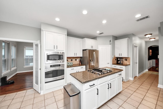 kitchen with light tile patterned flooring, a kitchen island, appliances with stainless steel finishes, white cabinets, and dark stone counters