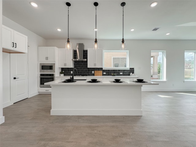 kitchen featuring a kitchen island with sink, decorative light fixtures, wall chimney exhaust hood, and appliances with stainless steel finishes