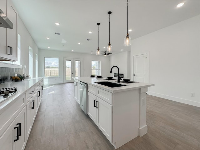 kitchen with decorative light fixtures, an island with sink, white cabinetry, sink, and stainless steel appliances