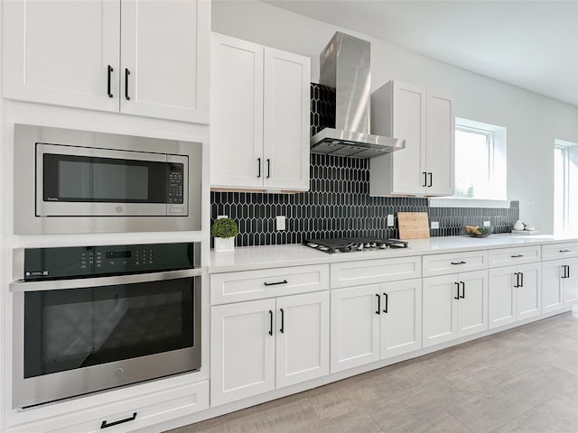 kitchen featuring wall chimney exhaust hood, white cabinetry, stainless steel appliances, and backsplash