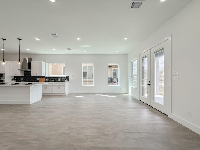 kitchen featuring french doors, wall chimney exhaust hood, hanging light fixtures, white cabinets, and backsplash